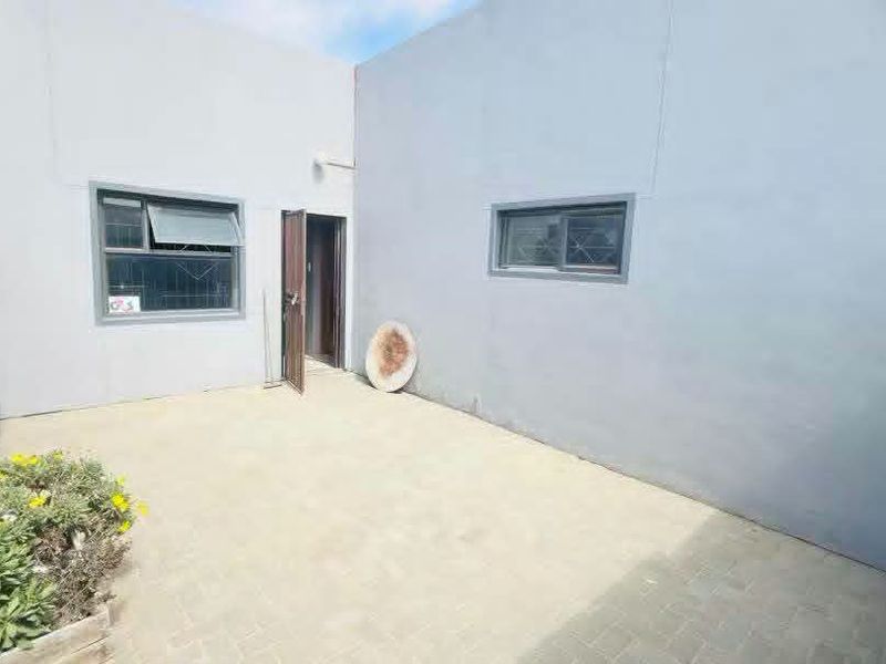 A paved rear courtyard area featuring grey rendered walls, security-fitted windows, and a single access door.