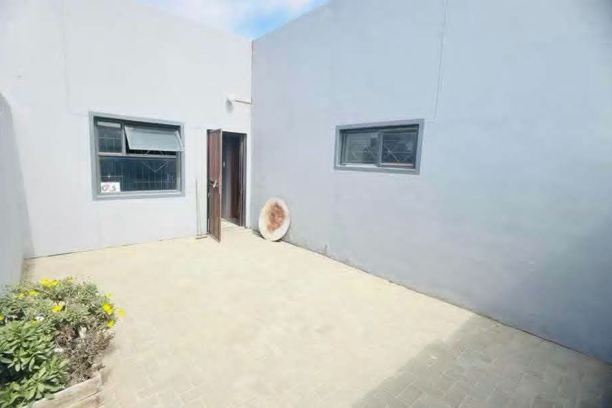 A paved rear courtyard area featuring grey rendered walls, security-fitted windows, and a single access door.