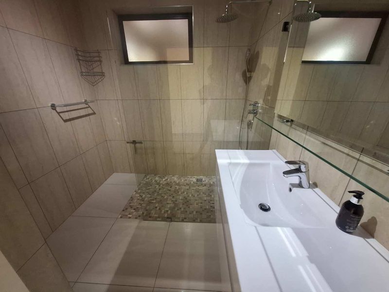 Modern bathroom featuring a walk-in shower with a rain shower head, mosaic floor detailing, and a sleek wall-mounted vanity unit.