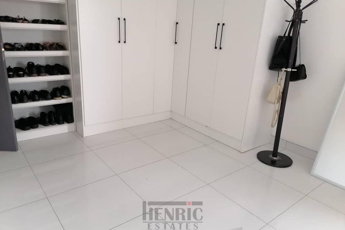 A clean bedroom featuring built-in white cabinetry and integrated open shelving for organized storage, finished with modern tiled flooring.