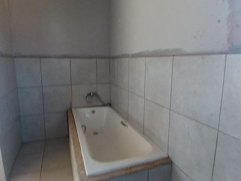 A bathroom featuring a built-in bathtub with tiled surround, currently in an unfinished state with exposed plaster walls.