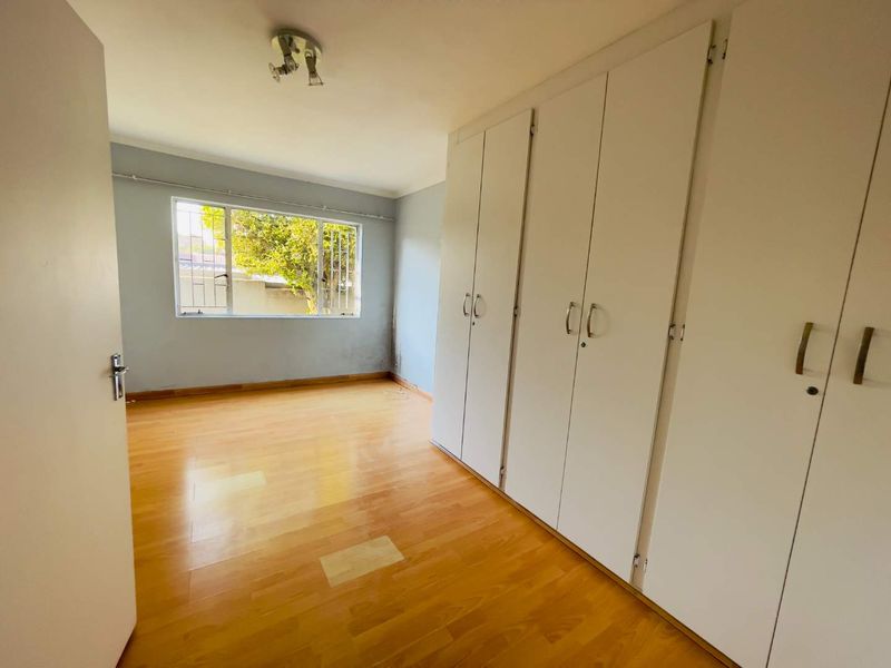 An empty bedroom featuring laminate flooring, built-in cupboards, and a window with security bars.