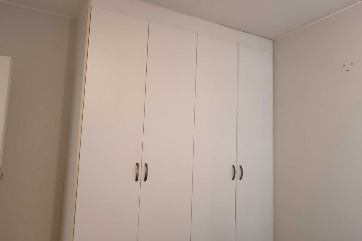 A clean bedroom featuring a floor-to-ceiling built-in wardrobe with white cabinetry and modern handles.