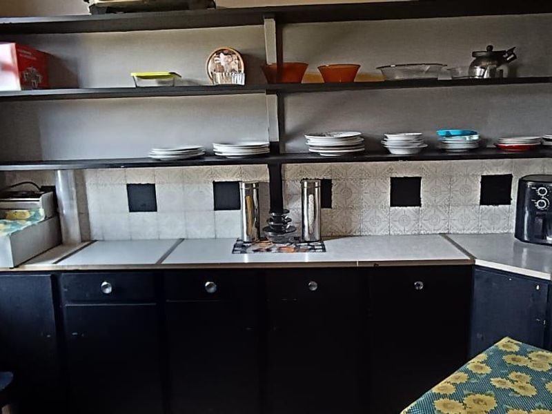 A functional scullery or pantry area featuring built-in black cabinetry, laminate countertops, and open shelving with a decorative tiled backsplash.