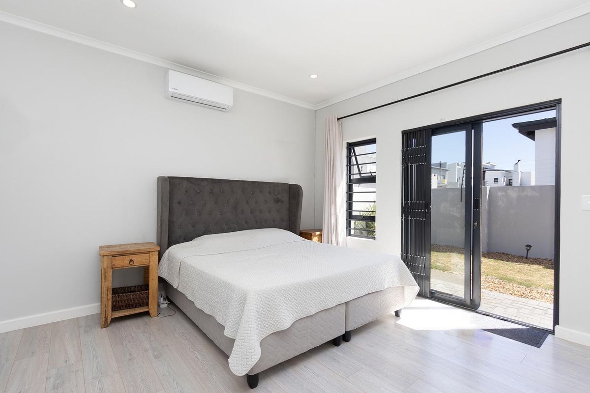 A bright bedroom featuring light wood-look flooring, a wall-mounted air conditioning unit, and sliding glass doors providing direct access to the rear garden.
