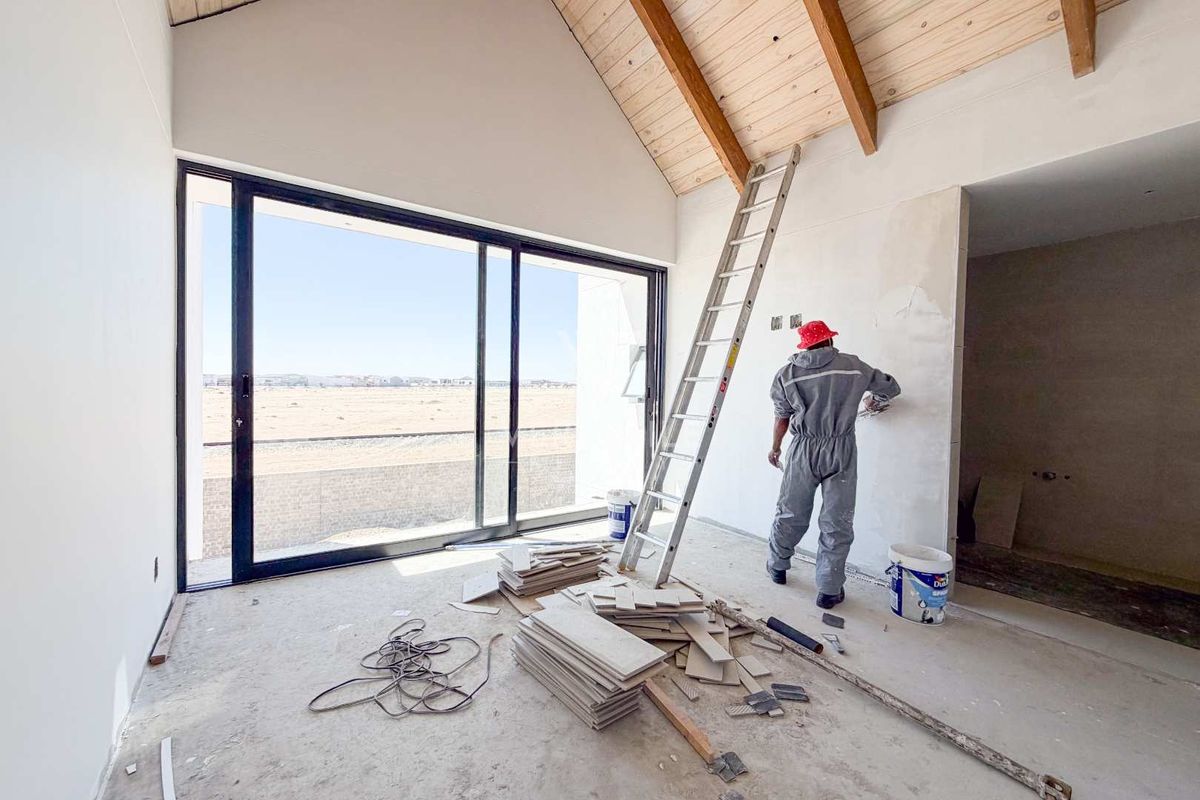 An unfinished living area featuring a high vaulted timber ceiling with exposed beams and large sliding glass doors leading to an outdoor view.