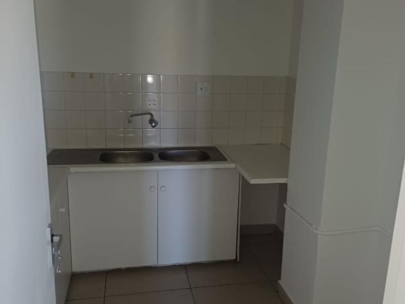 A compact office kitchenette featuring a double sink, tiled backsplash, and built-in white cabinetry with tiled flooring.