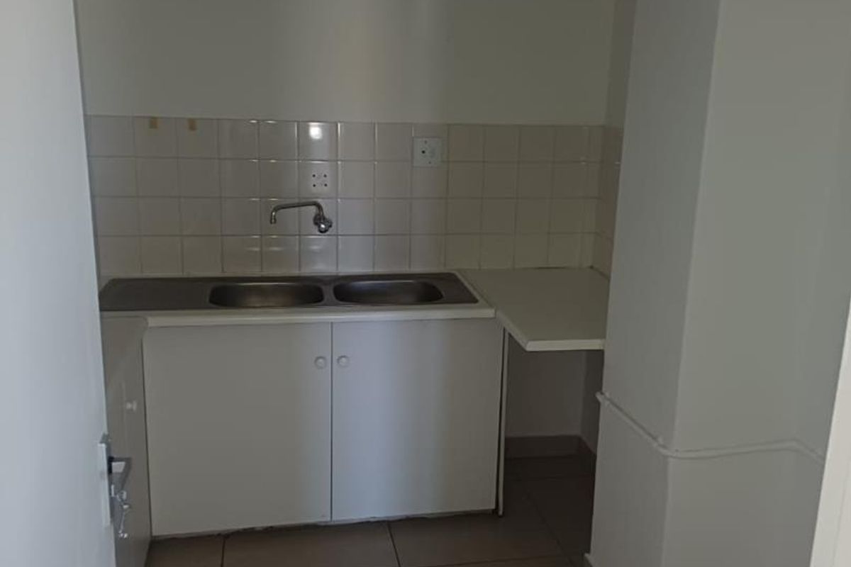 A compact office kitchenette featuring a double sink, tiled backsplash, and built-in white cabinetry with tiled flooring.