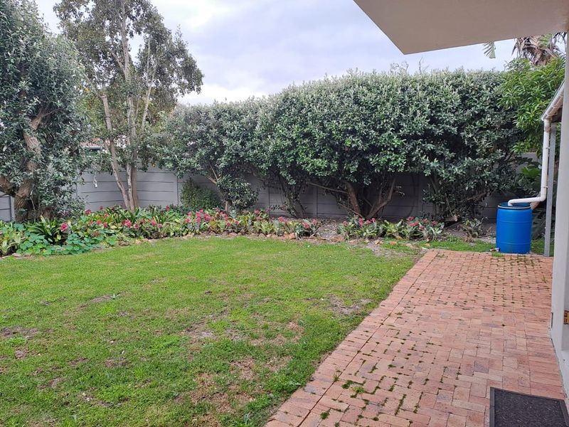 A private rear garden featuring a brick-paved patio area, established perimeter hedging, and a lawn with a rainwater collection system.