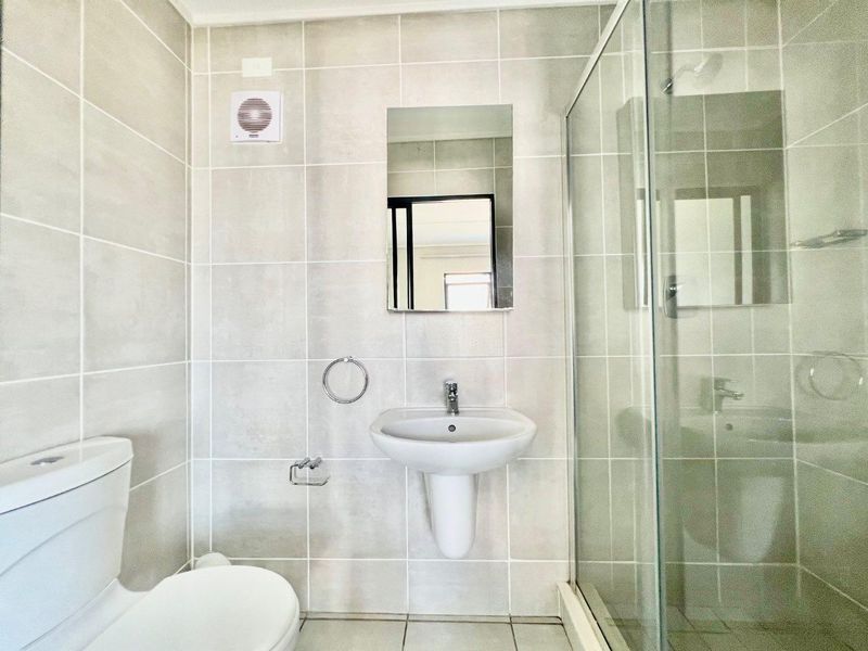 A clean, modern bathroom featuring a pedestal basin, a glass-enclosed shower, and neutral wall tiling.