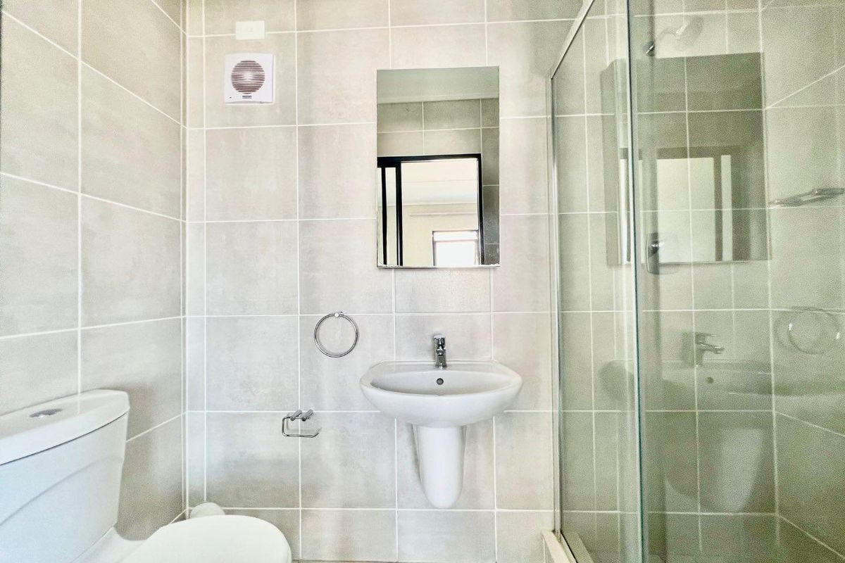 A clean, modern bathroom featuring a pedestal basin, a glass-enclosed shower, and neutral wall tiling.