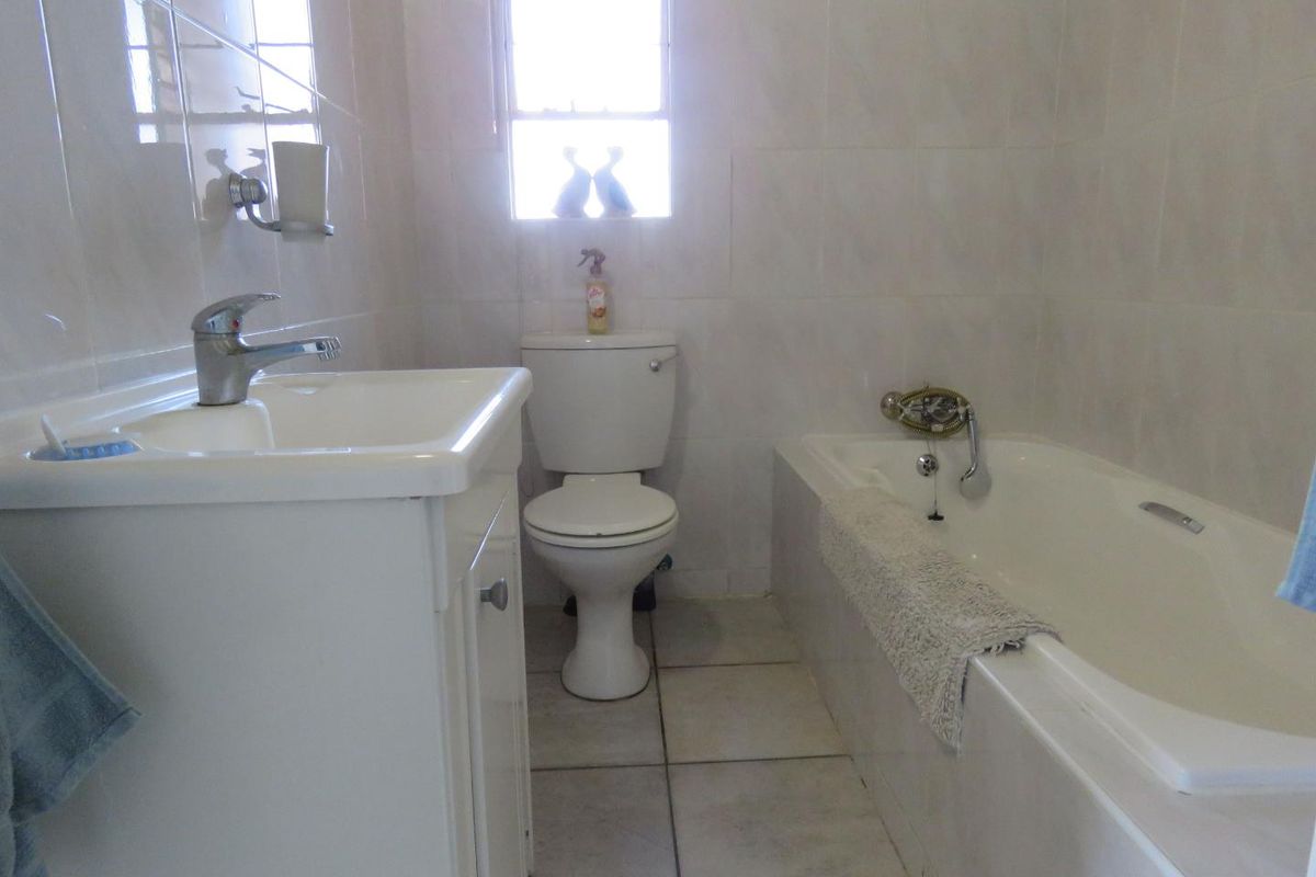A functional bathroom featuring a built-in bathtub, a pedestal vanity with a basin, and a standard toilet, finished with neutral wall and floor tiles.