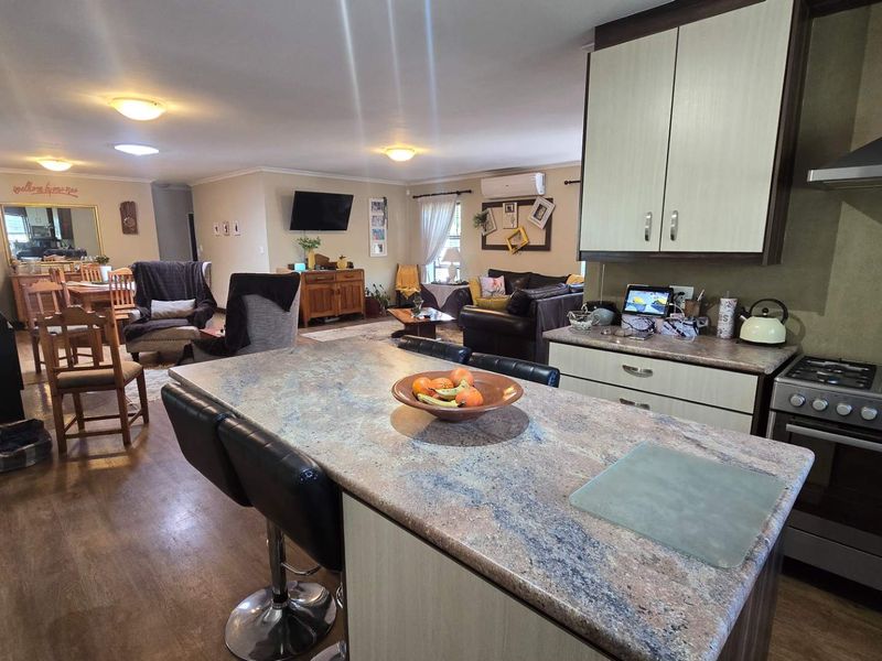 Spacious open-plan living area featuring a functional kitchen with stone-topped island, gas stove, and a cozy wood-burning fireplace in the adjacent lounge space.