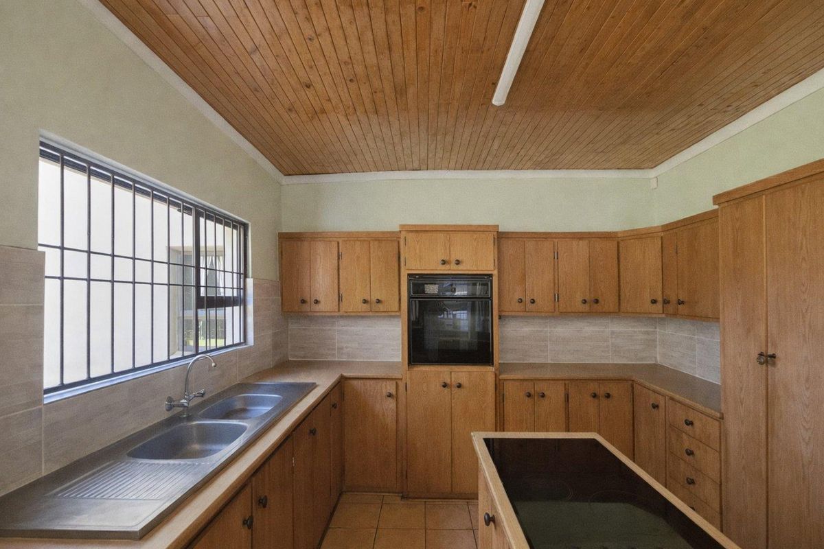 A functional kitchen featuring wooden cabinetry, a built-in oven, a ceramic hob on the island, and a double stainless steel sink.