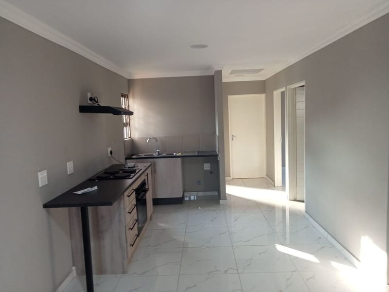 A modern, empty kitchen featuring sleek built-in cabinetry, a dark laminate countertop, integrated hob and oven, and polished white tiled flooring.