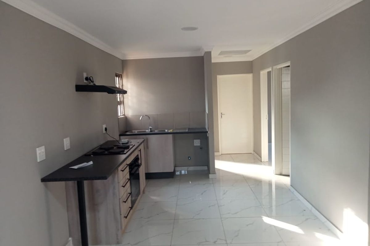 A modern, empty kitchen featuring sleek built-in cabinetry, a dark laminate countertop, integrated hob and oven, and polished white tiled flooring.