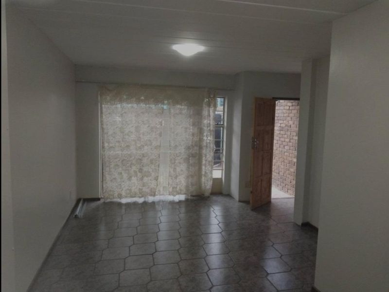 An empty living room featuring tiled flooring and a sliding glass door leading to an outdoor area.