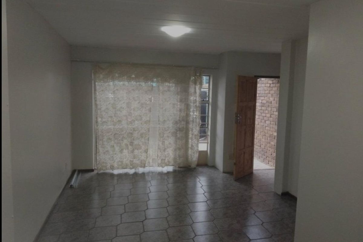 An empty living room featuring tiled flooring and a sliding glass door leading to an outdoor area.