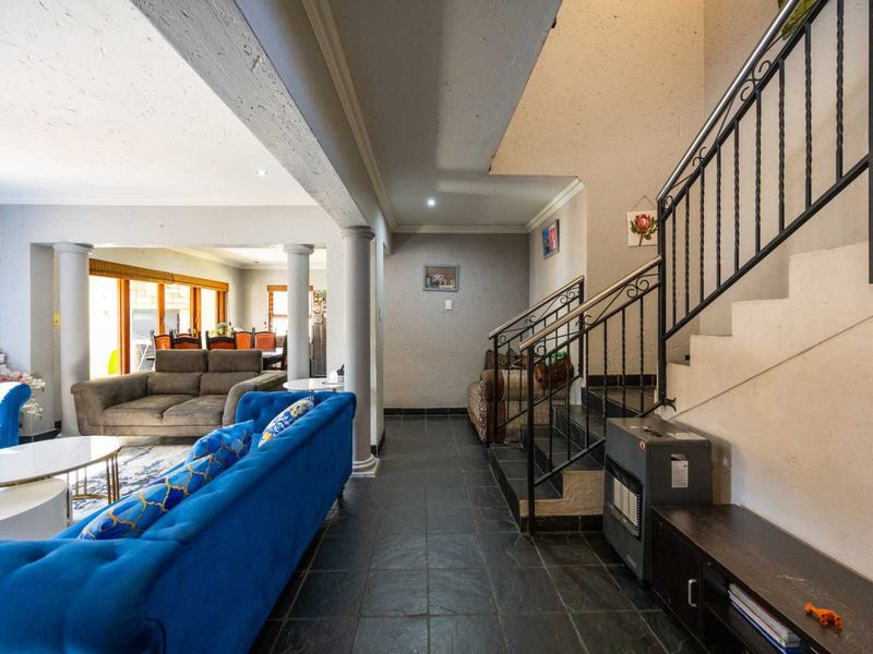 Open plan living area featuring a wrought iron staircase, tiled flooring, and structural columns, creating a spacious and connected layout.