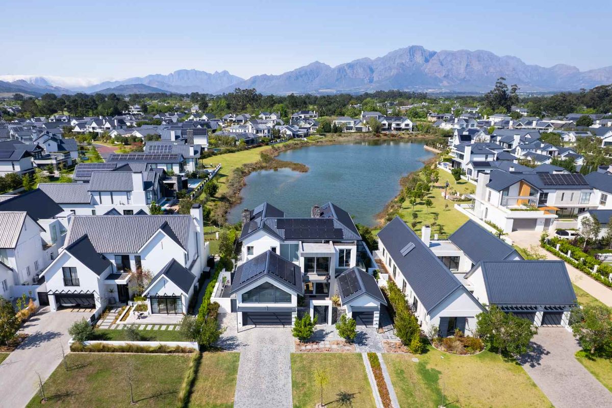 Aerial view of a modern residential estate featuring contemporary homes with metal roofs, solar panels, and landscaped gardens overlooking a central lake.