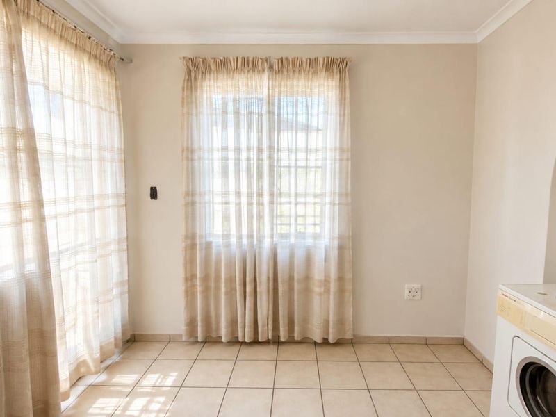 A functional laundry area featuring tiled flooring, neutral walls, and natural light from large windows, providing a clean and practical utility space.