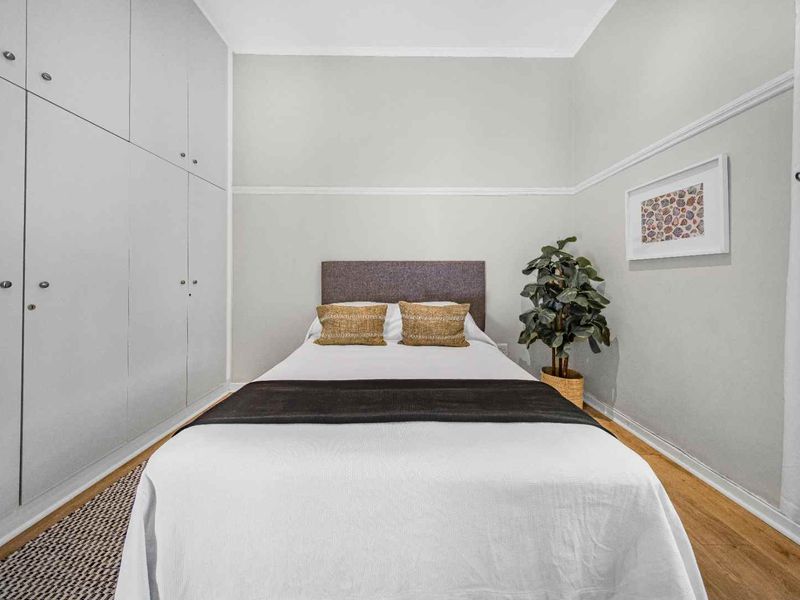 A well-maintained bedroom featuring light-toned walls, timber flooring, and extensive floor-to-ceiling built-in cupboards for ample storage.