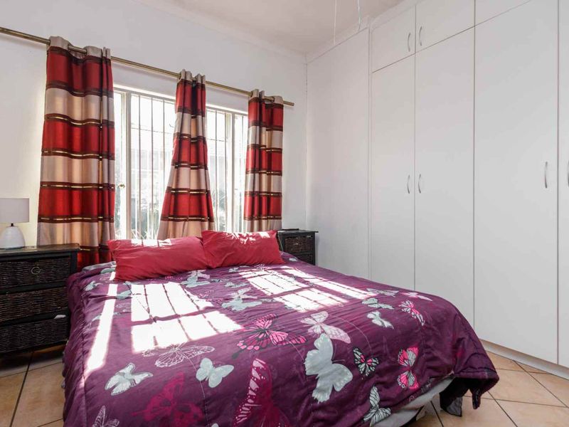A functional bedroom featuring built-in cupboards, tiled flooring, and security bars on the window, providing a practical and secure living space.