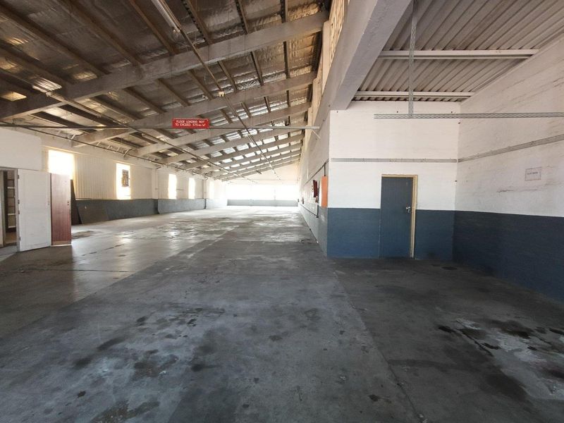 Spacious industrial utility area featuring exposed steel roof trusses, concrete flooring, and functional metal wall cladding, suitable for storage or workshop use.