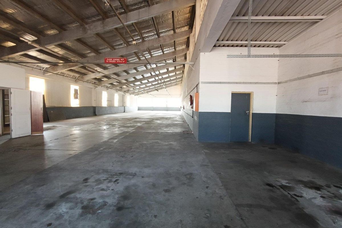 Spacious industrial utility area featuring exposed steel roof trusses, concrete flooring, and functional metal wall cladding, suitable for storage or workshop use.