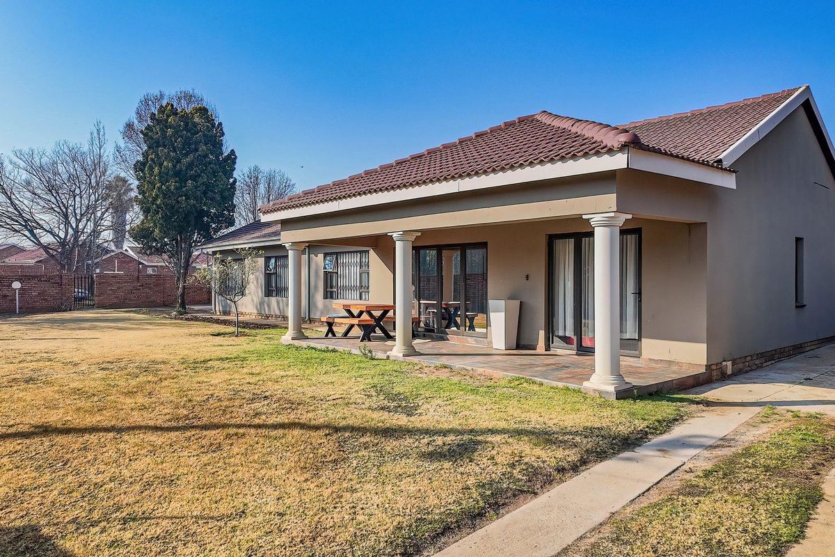 Rear view of the house featuring a spacious covered patio with concrete columns, tiled roof, and access to the garden via sliding glass doors.