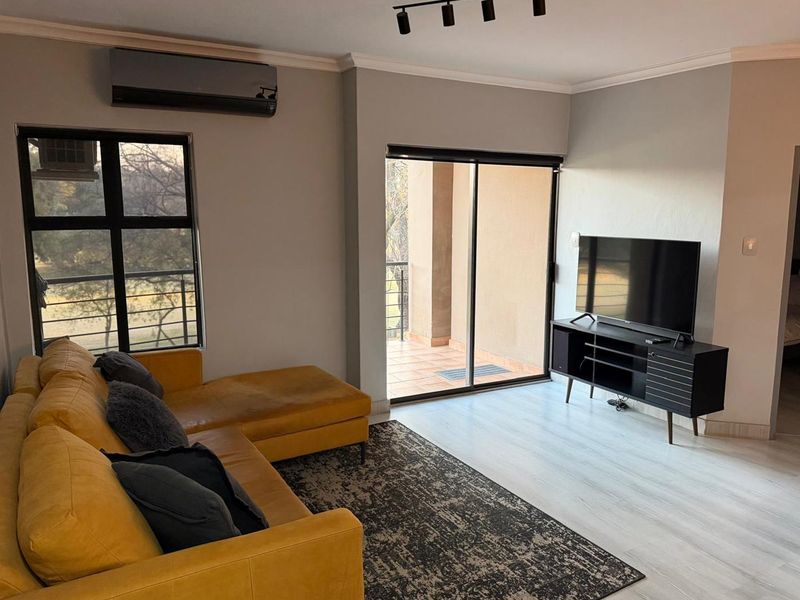 A well-maintained living room featuring laminate flooring, track lighting, a split-system air conditioner, and direct access to a private balcony through sliding glass doors.