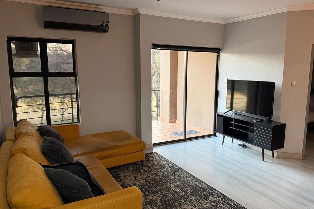 A well-maintained living room featuring laminate flooring, track lighting, a split-system air conditioner, and direct access to a private balcony through sliding glass doors.
