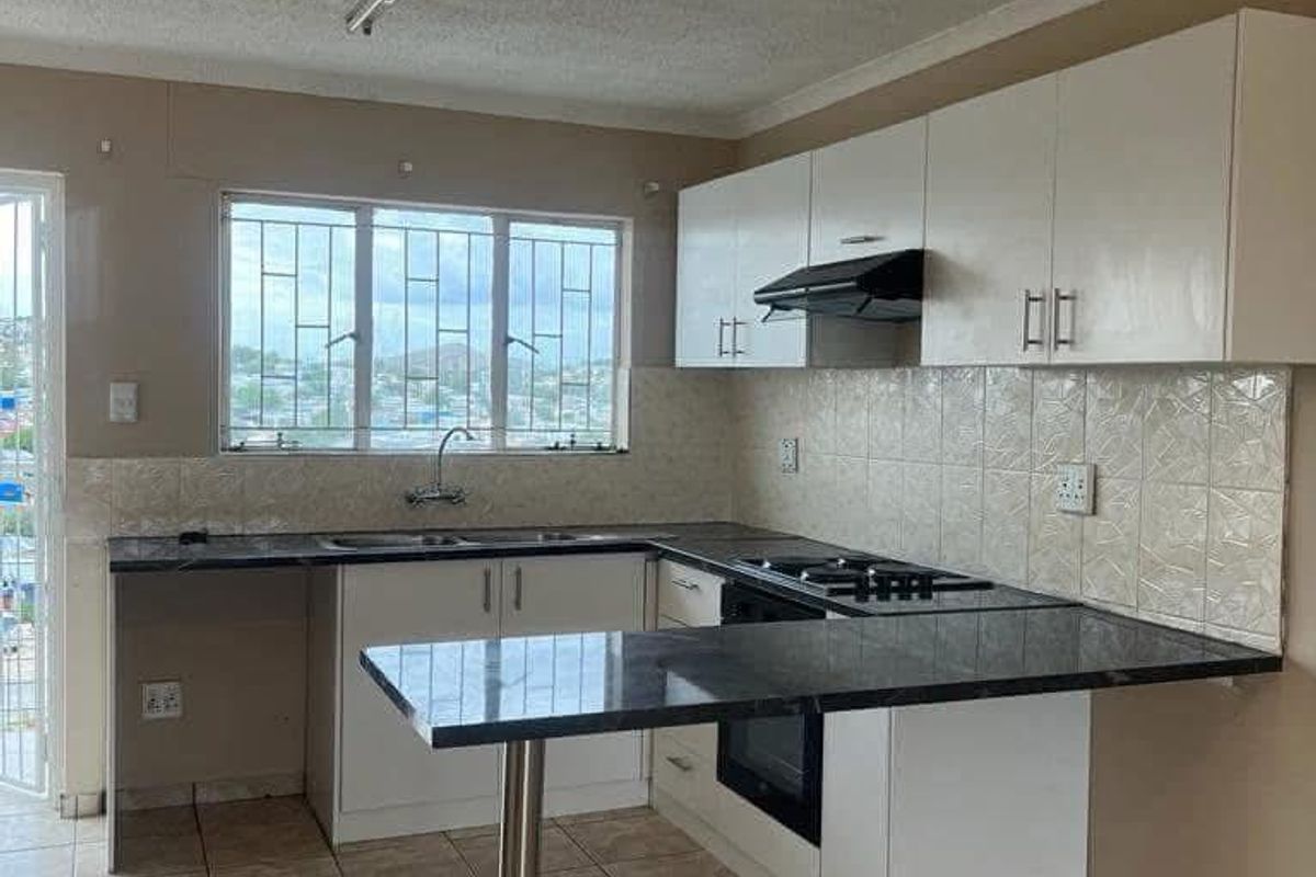 Functional kitchen featuring white cabinetry, dark granite countertops, built-in oven, hob, extractor fan, and tiled flooring with a breakfast bar extension.
