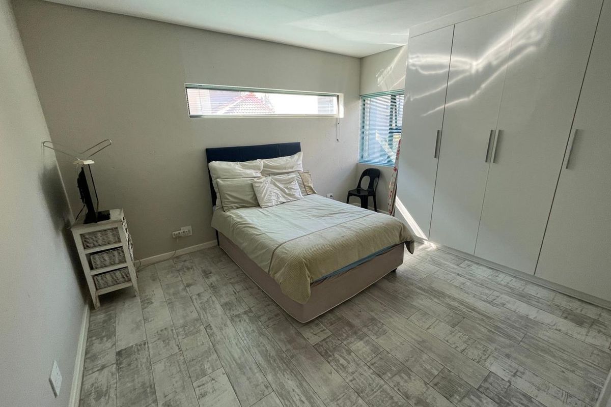 A well-lit bedroom featuring modern wood-look tile flooring, built-in floor-to-ceiling wardrobes, and a combination of horizontal and standard windows.