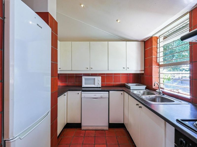 A functional kitchen featuring white cabinetry, dark laminate countertops, a double sink, and distinctive red tiled walls and flooring.