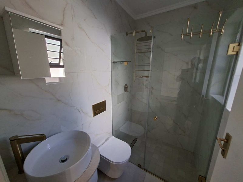 Modern bathroom featuring marble-look wall tiles, a glass-enclosed shower with brass fixtures, a vessel sink, and a wall-mounted toilet.