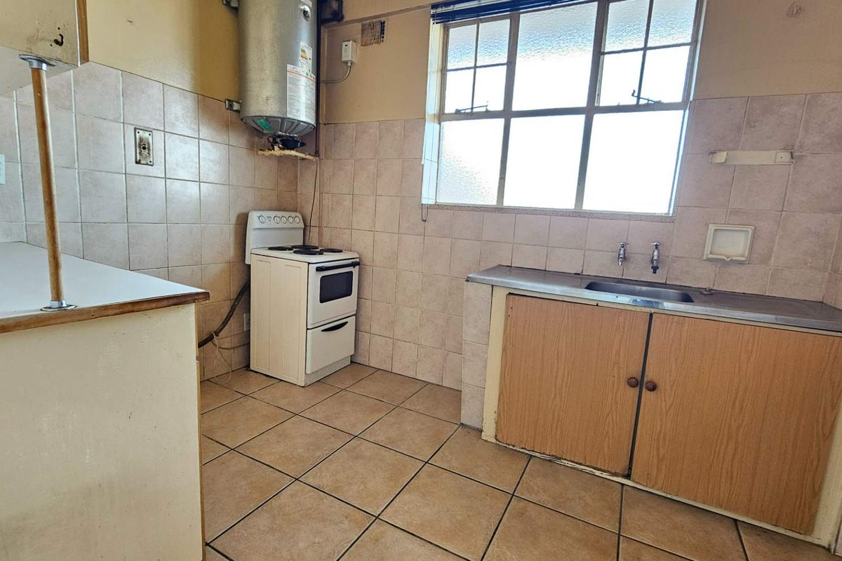 A functional kitchen featuring tiled walls, a stainless steel sink, built-in cabinetry, and a freestanding stove, offering potential for modernization.