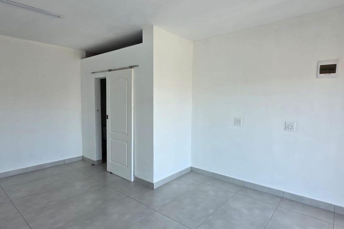 A clean, empty open-plan retail or office space featuring neutral tiled flooring, white walls, and convenient plumbing and electrical access points.