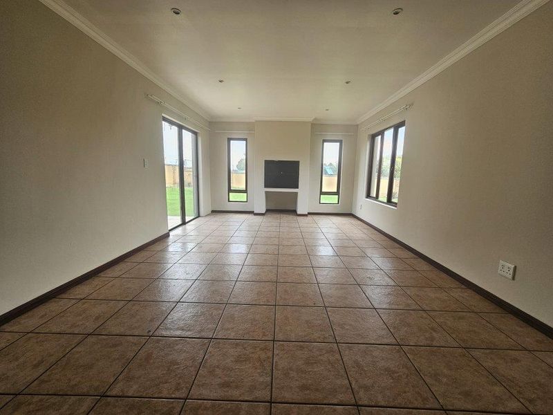 Spacious, empty living room featuring tiled flooring, a central built-in fireplace, and large windows providing ample natural light and garden access.