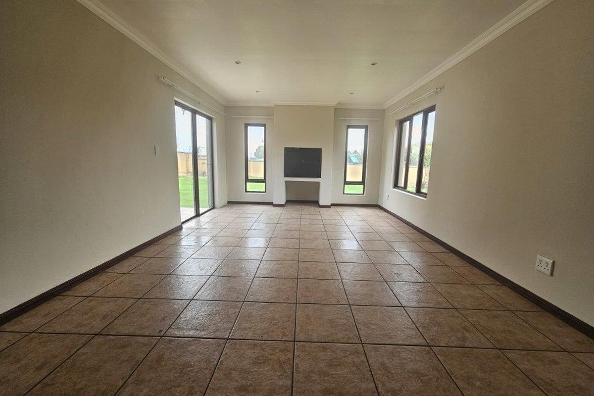 Spacious, empty living room featuring tiled flooring, a central built-in fireplace, and large windows providing ample natural light and garden access.