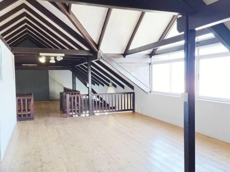 Spacious loft-style living area featuring high vaulted ceilings with exposed timber beams, polished wooden floors, and a timber balustrade overlooking the lower level.
