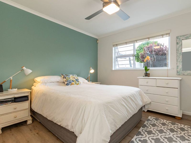 A well-maintained bedroom featuring a green accent wall, ceiling fan, and louver window providing natural light.