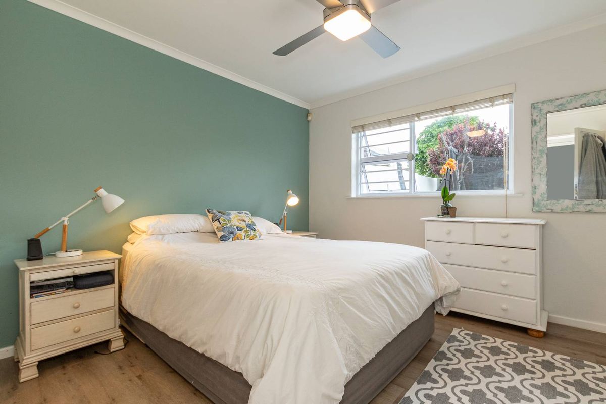 A well-maintained bedroom featuring a green accent wall, ceiling fan, and louver window providing natural light.