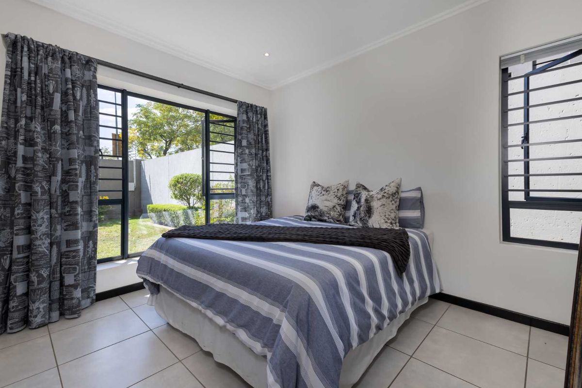 A bright bedroom featuring tiled flooring, large windows with security bars, and direct access to a private garden area.