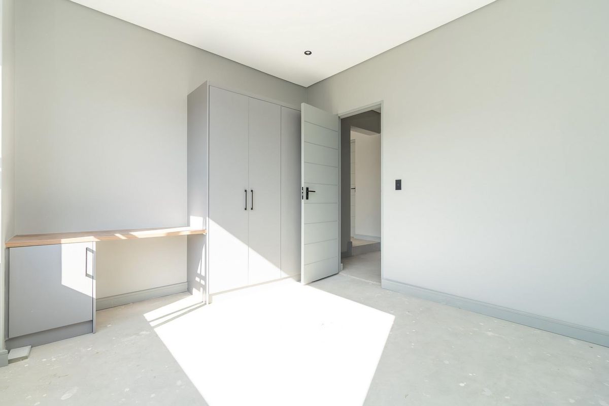 A bright, modern bedroom featuring built-in cabinetry, a fitted desk area, and neutral finishes, ready for final flooring installation.