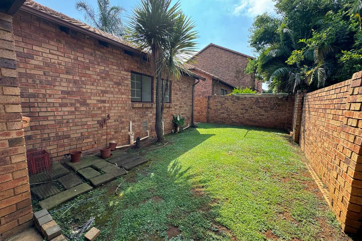 A private rear garden area featuring face brick exterior walls, a perimeter boundary wall, and a small paved section.