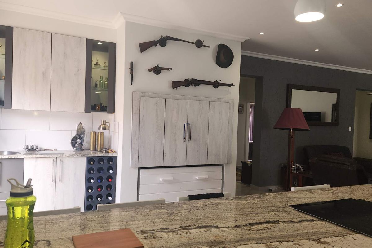 A modern kitchen featuring granite countertops, integrated cabinetry, a built-in wine rack, and recessed lighting, seamlessly flowing into the adjacent living area.