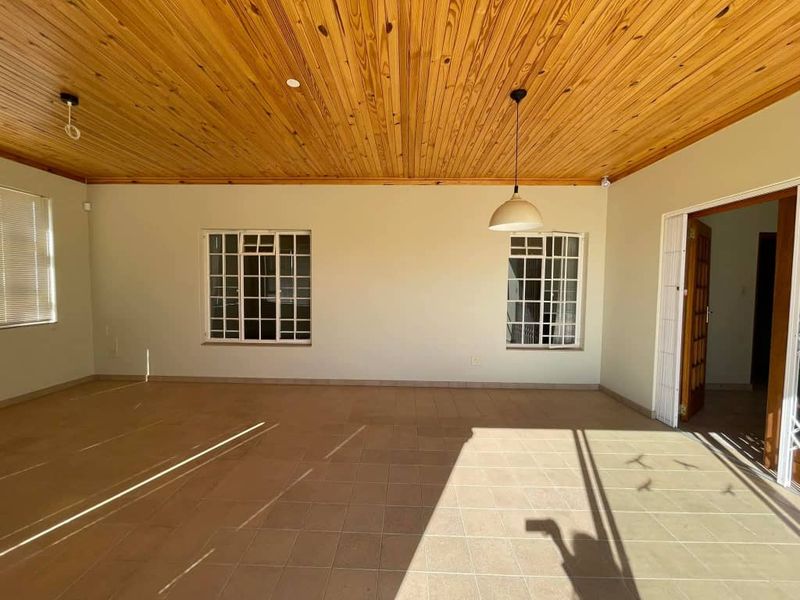 A spacious, empty covered patio featuring a warm timber tongue and groove ceiling, tiled flooring, and security-fitted windows.