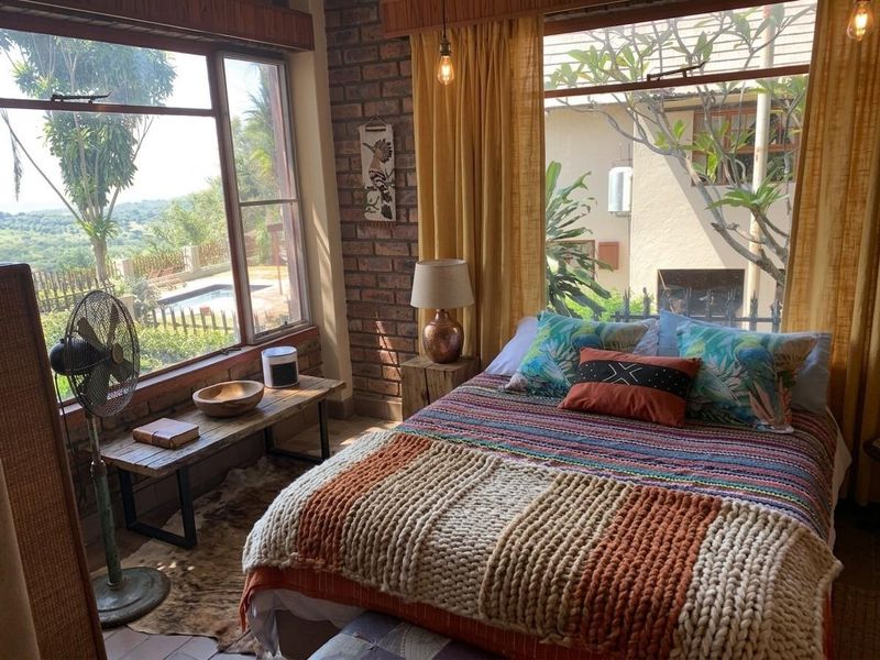 A cozy bedroom featuring exposed brick walls, large windows providing natural light, and views of the outdoor pool area.