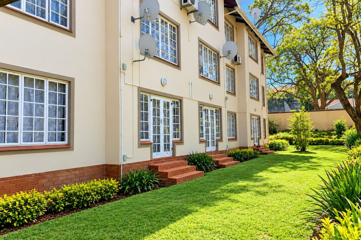 A well-maintained rear exterior view of an apartment complex featuring brick plinth detailing, multi-pane windows, french doors, and a lush, manicured garden.